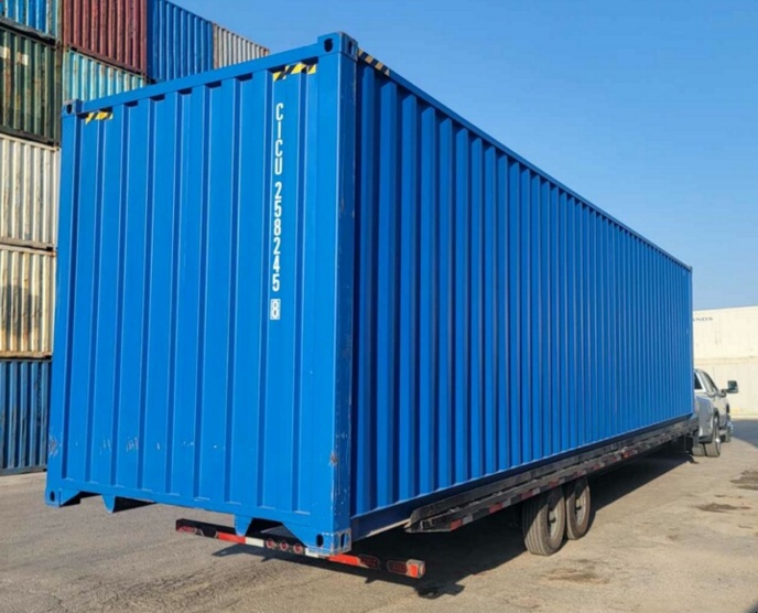A blue shipping container loaded on a delivery trailer at a depot