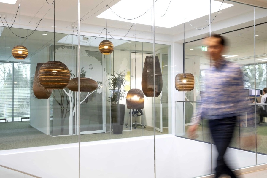 Pendant lamps and glass meeting rooms in BOM’s offices, with a person walking past