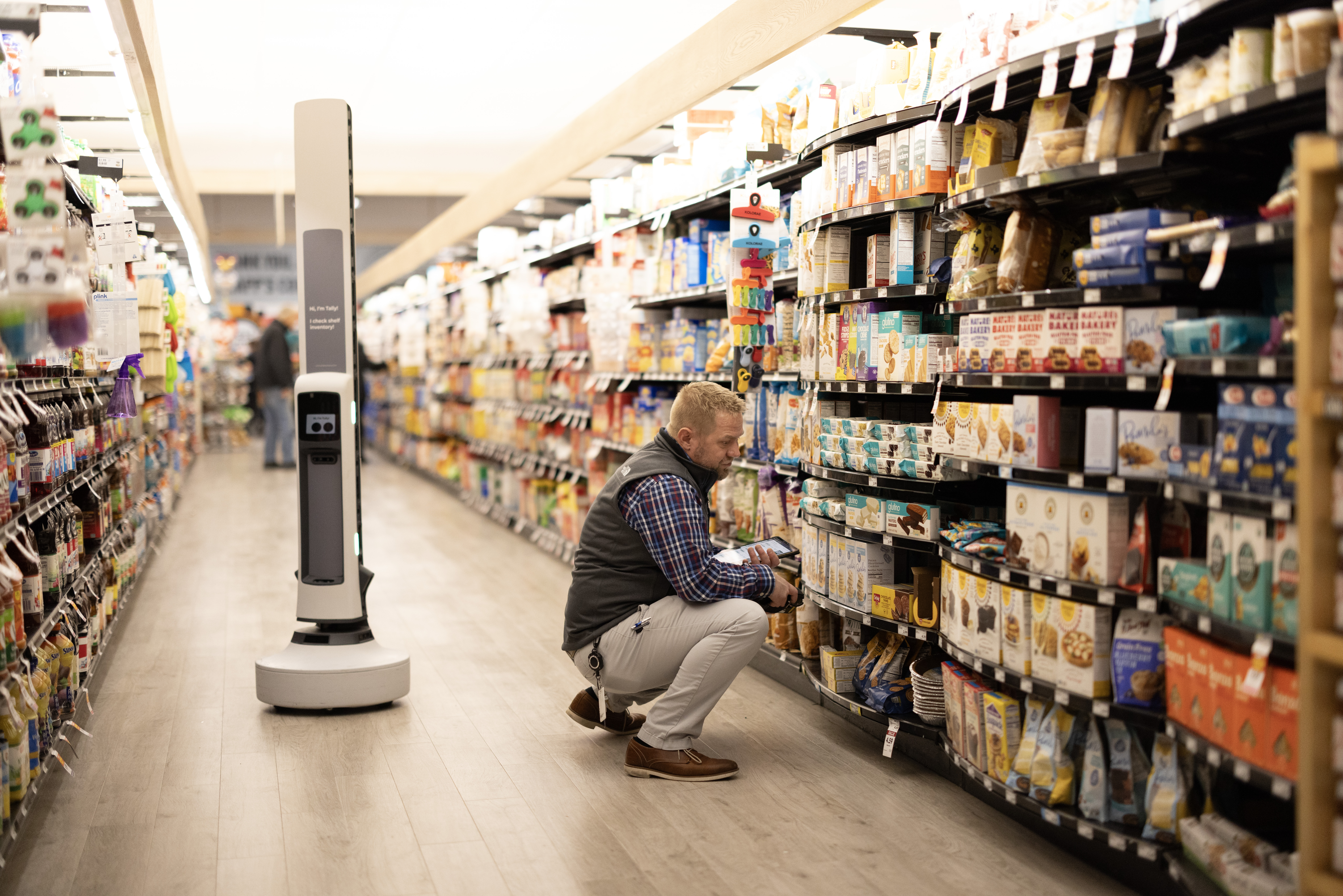 Tally beside a person checking a tablet in a supermarket aisle