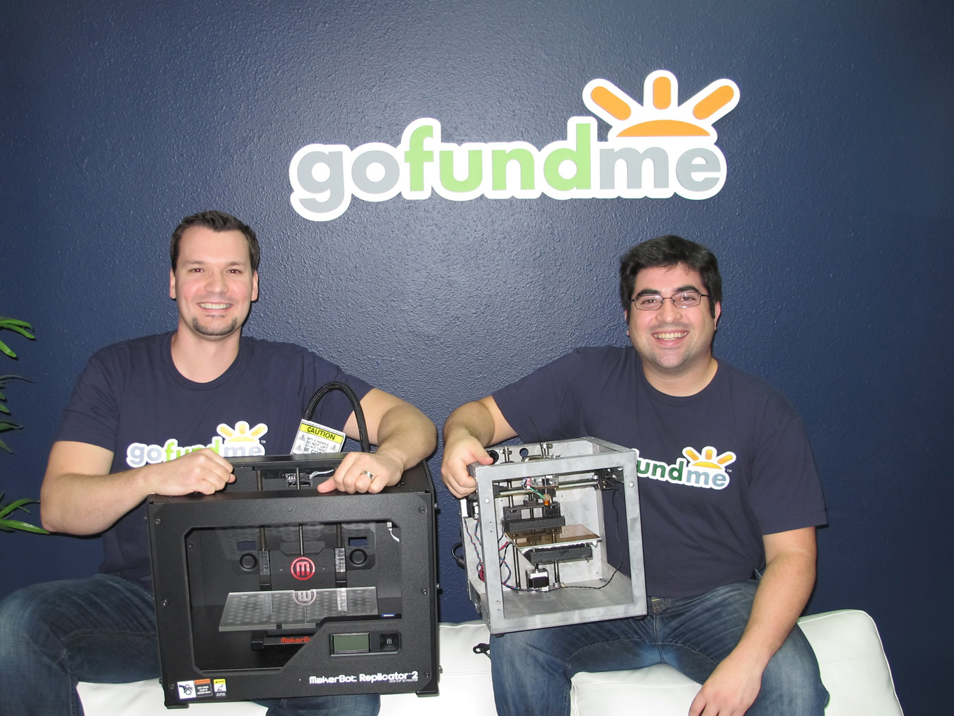 Brad Damphousse on the left and Andy Ballester on the right, each holding a 3D printer beneath a GoFundMe sign.