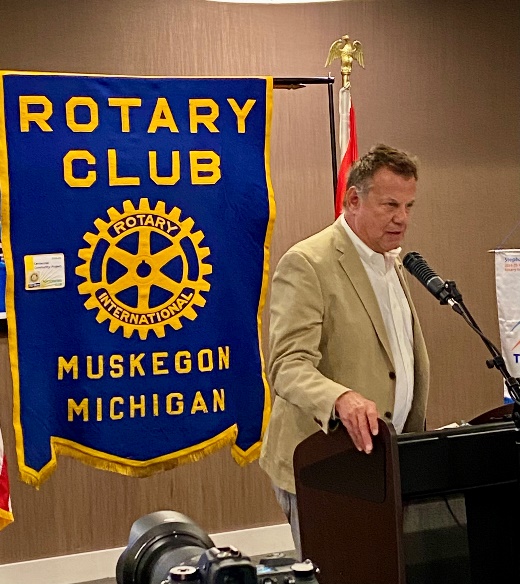 Brad Playford speaking beside the Muskegon Rotary Club banner