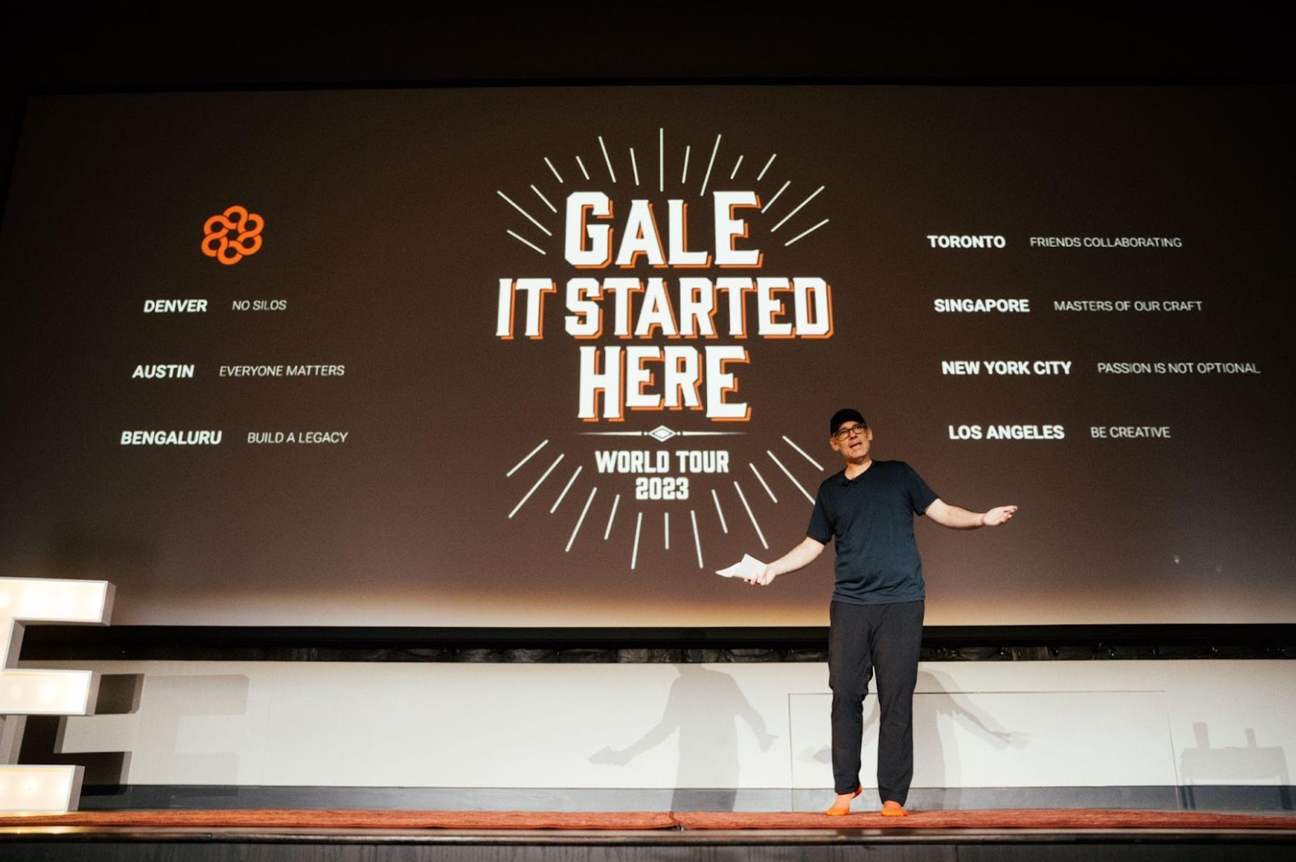 Brad Simms presenting GALE's 2023 world tour in front of a screen listing offices and company values