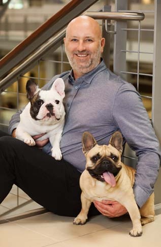 Brad Weston seated on a staircase, smiling with two French bulldogs