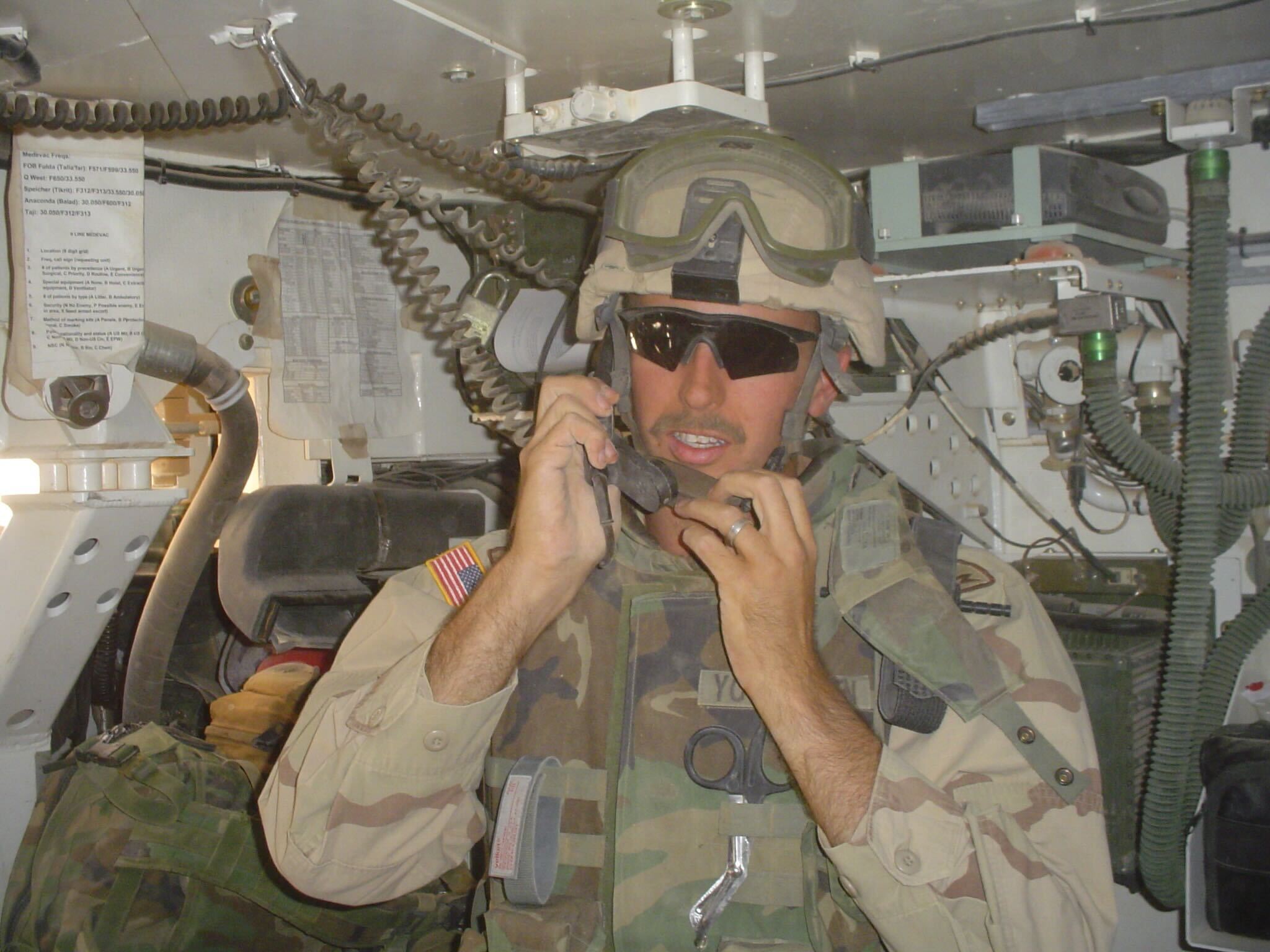 Brad Younggren in U.S. Army gear speaking on a field telephone inside a military vehicle
