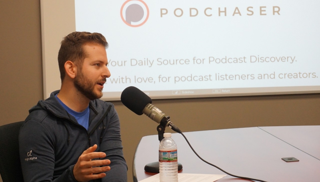 Bradley Davis speaking into a microphone with a Podchaser presentation behind him