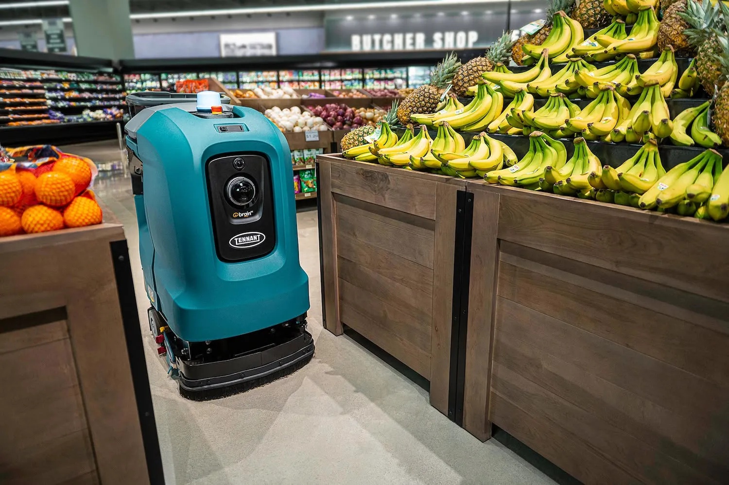 A Tennant X4 ROVR autonomous floor scrubber beside a grocery store produce display