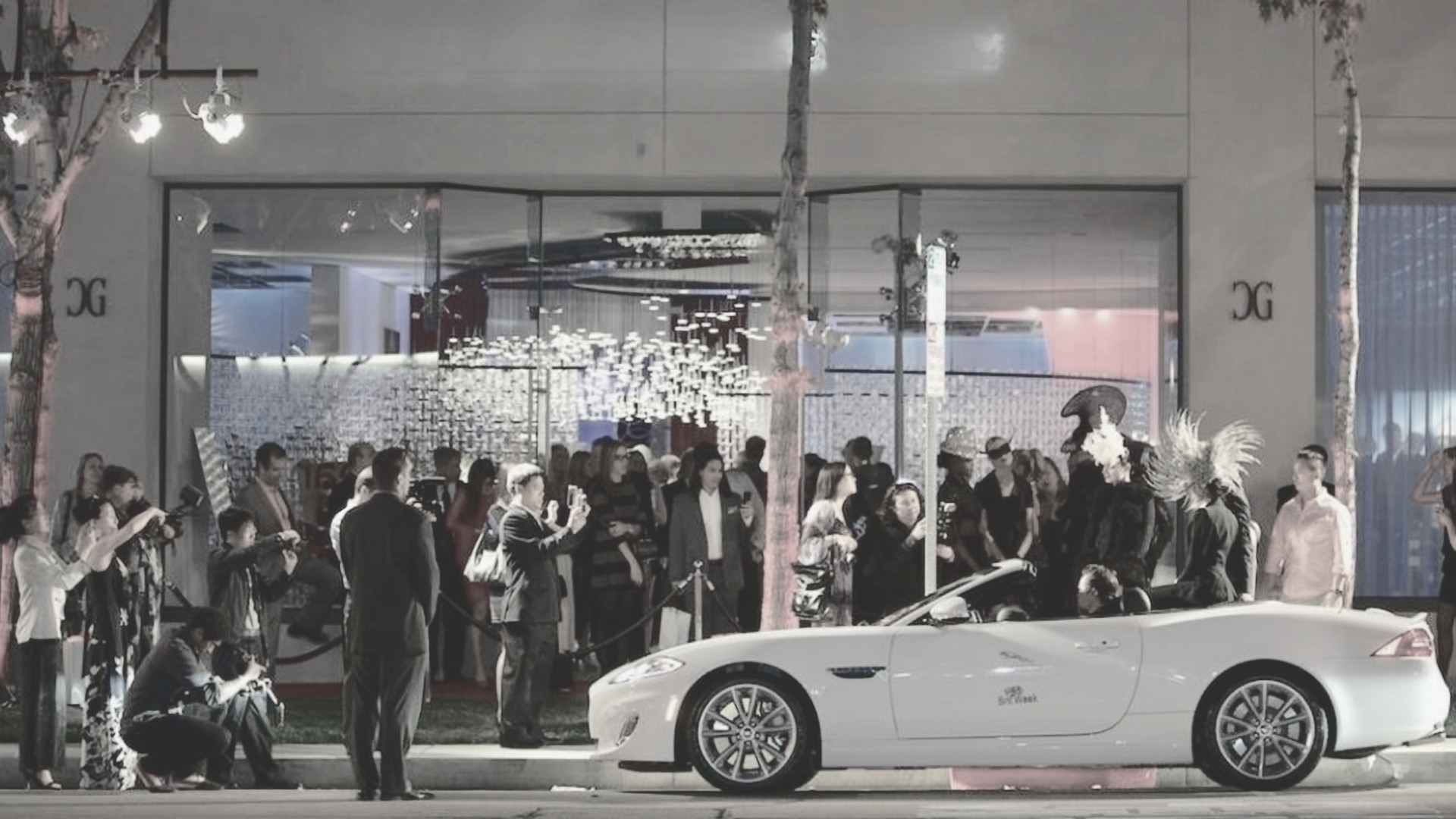 Crowd outside a luxury furniture showroom with a white convertible parked in front