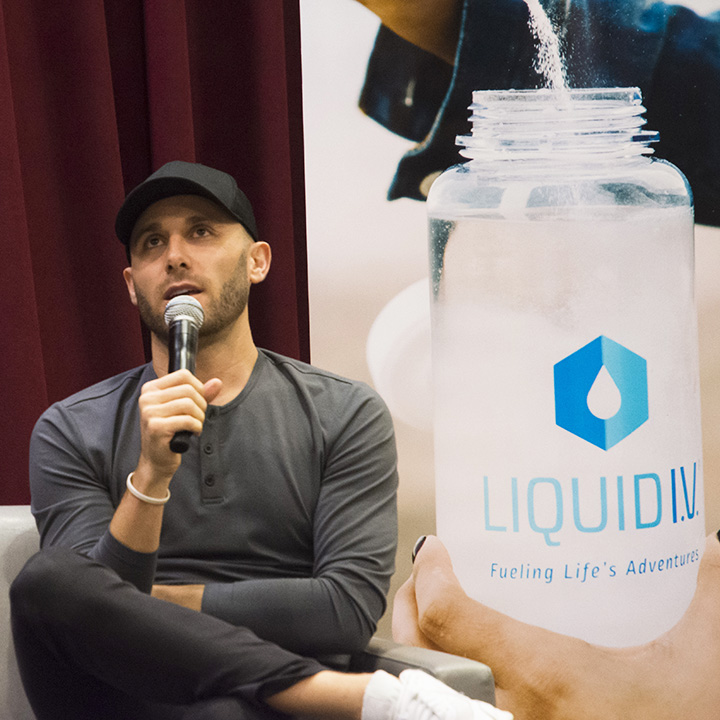 Brandin Cohen seated with a microphone beside a Liquid I.V. display at an LMU entrepreneurship event