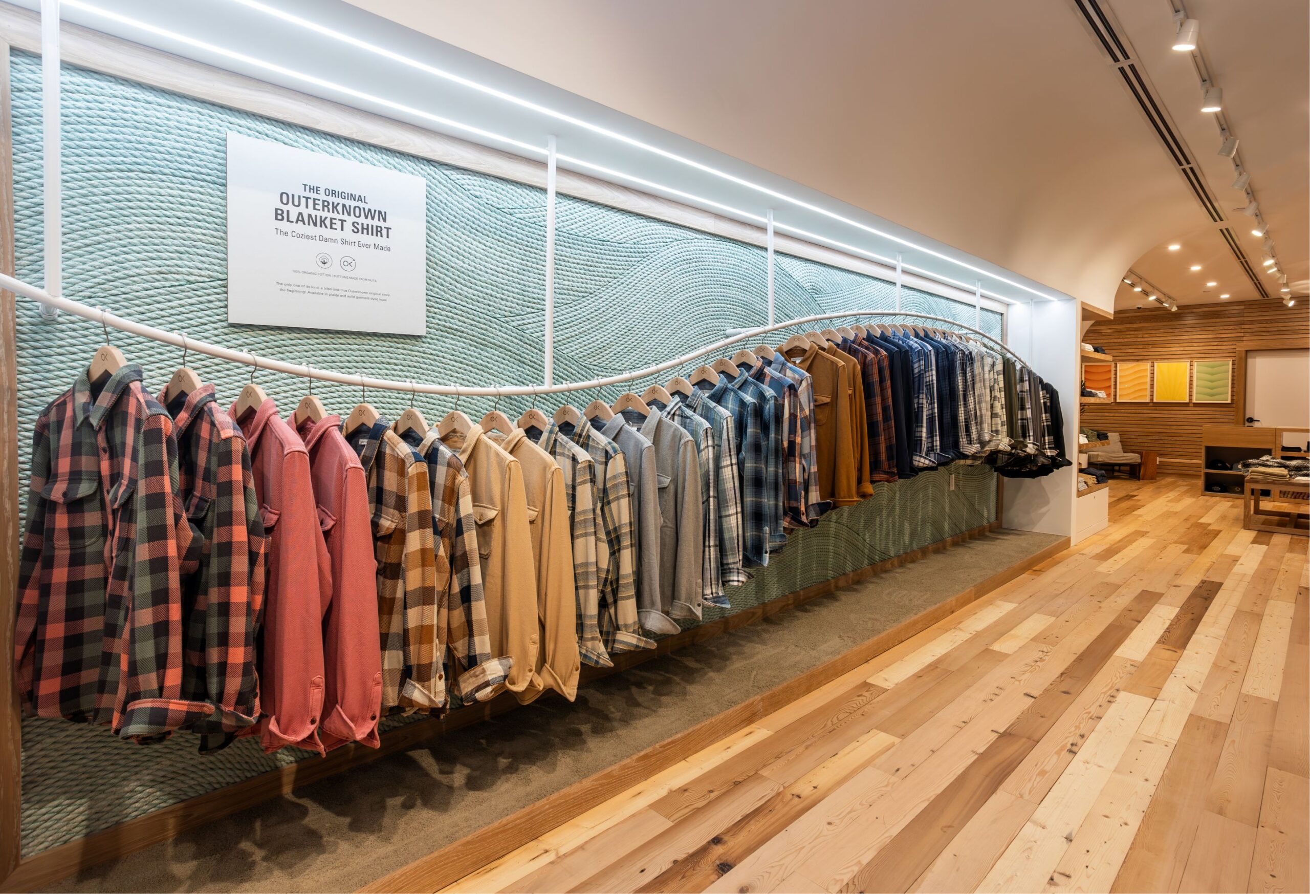 Outerknown shirts arranged along a curved rail against a textured wall in a Starch-designed store