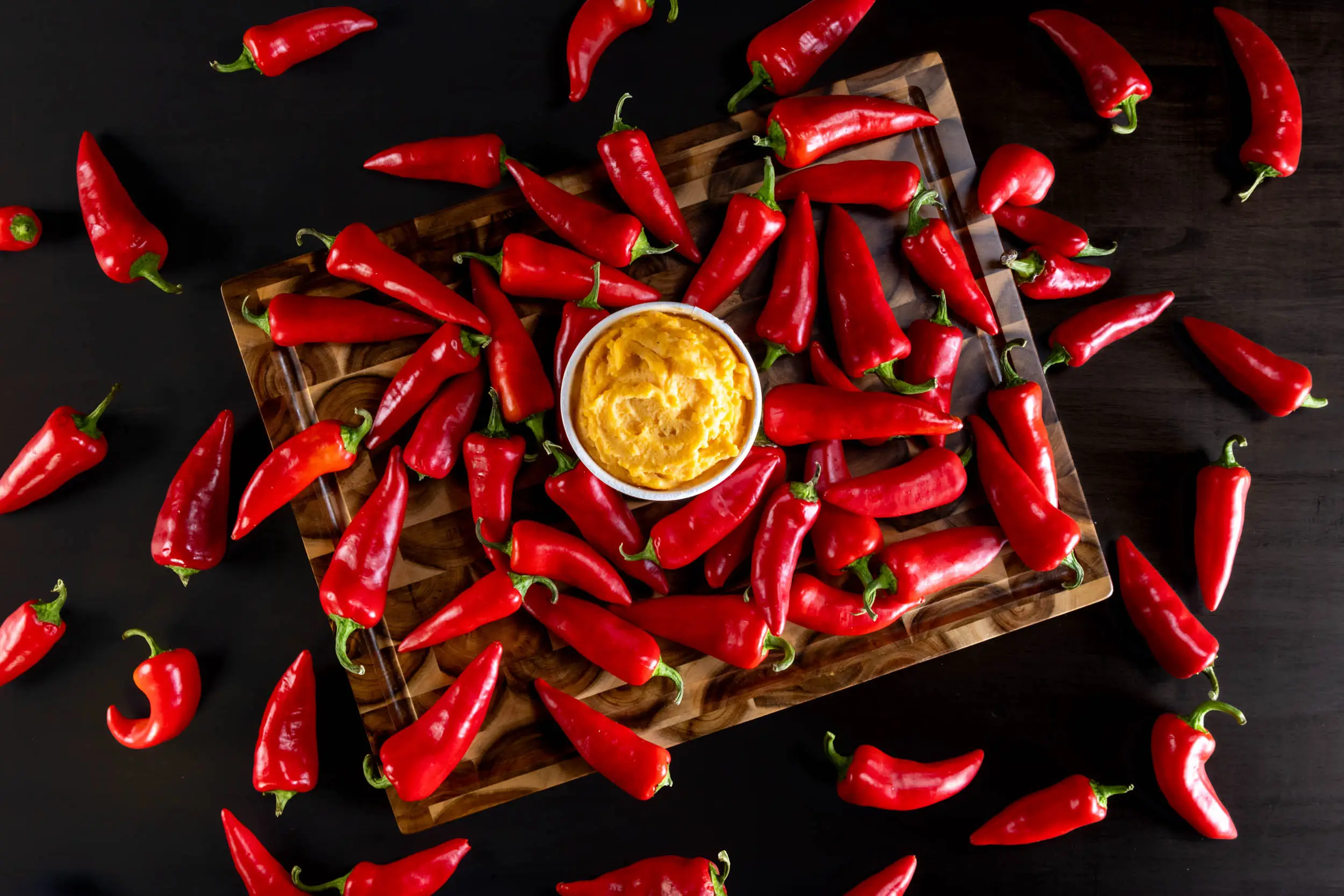 A bowl of mashed potatoes surrounded by bright red peppers