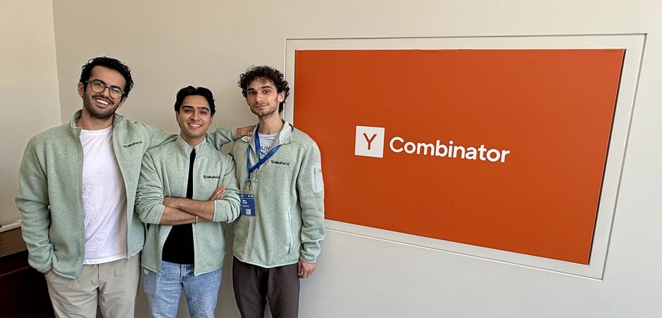 The three MindFort co-founders standing beside a Y Combinator sign in matching pale-green jackets