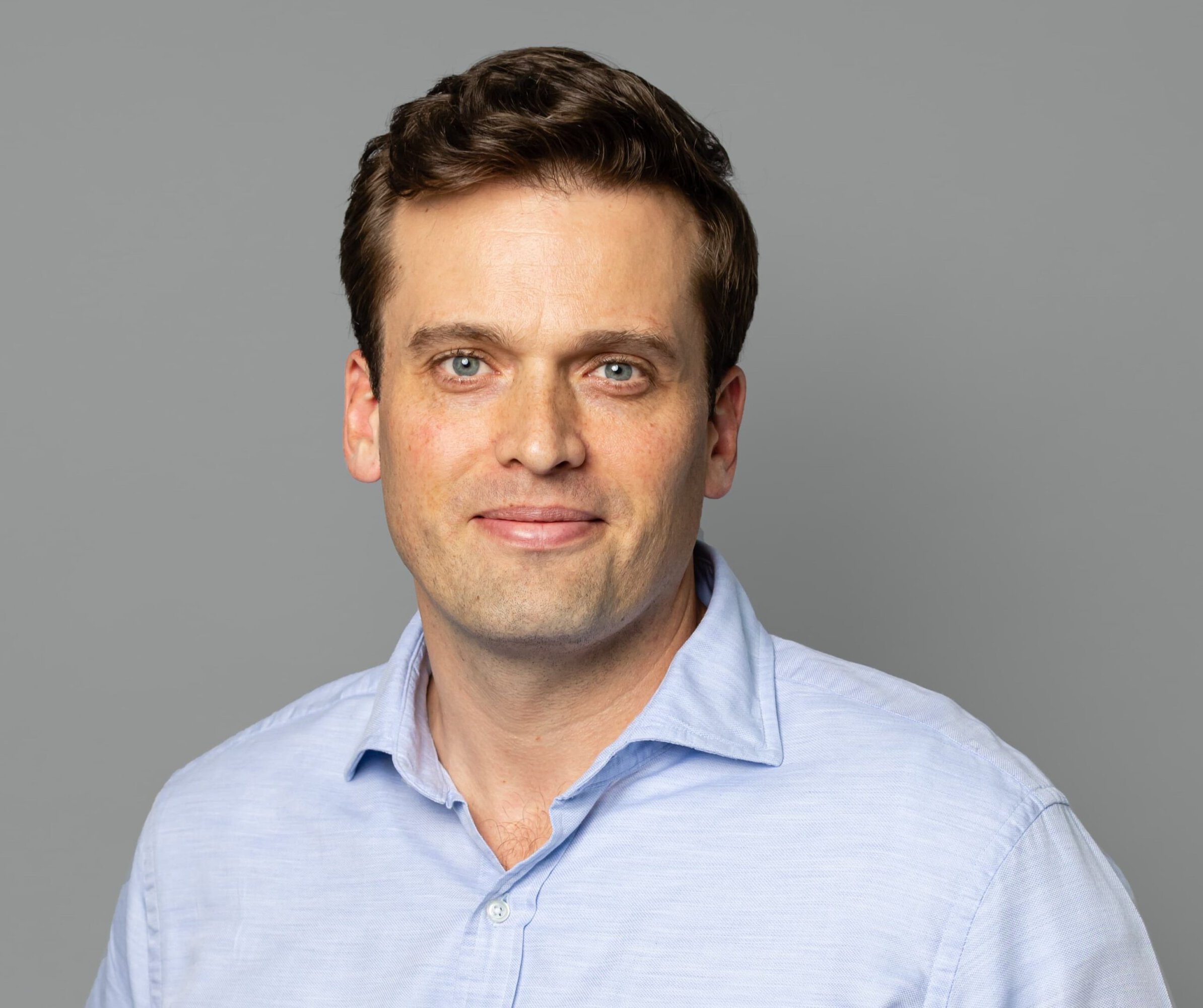 Branigan Mulcahy in a light blue shirt against a gray studio background