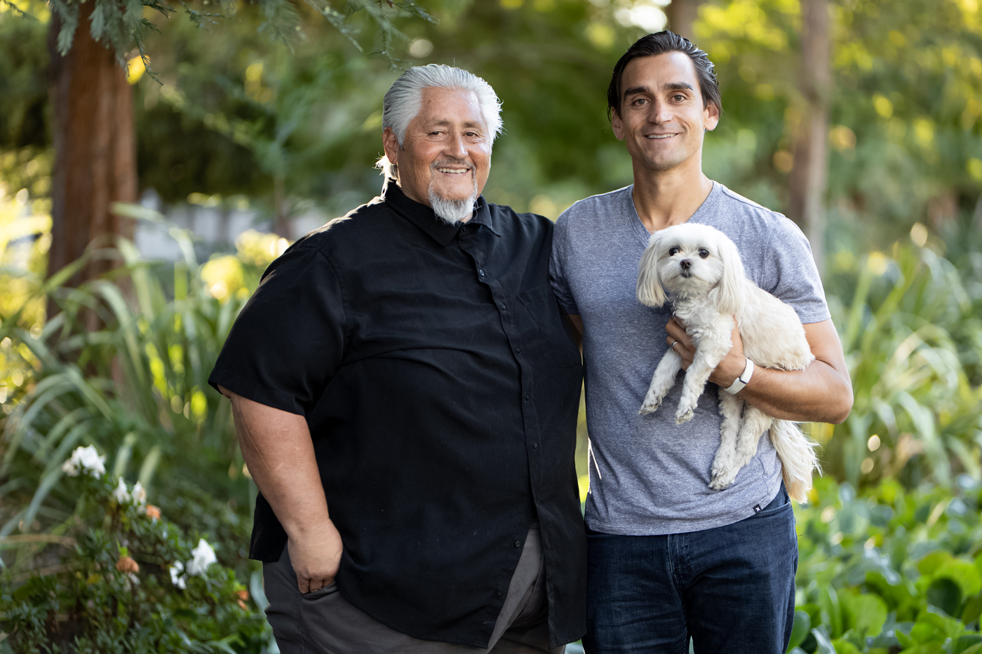 Dan Arriola and Daniel Arriola standing outdoors with a small white dog