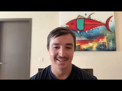 Brendan Burnett speaking in a video interview, with a colorful fish painting behind him