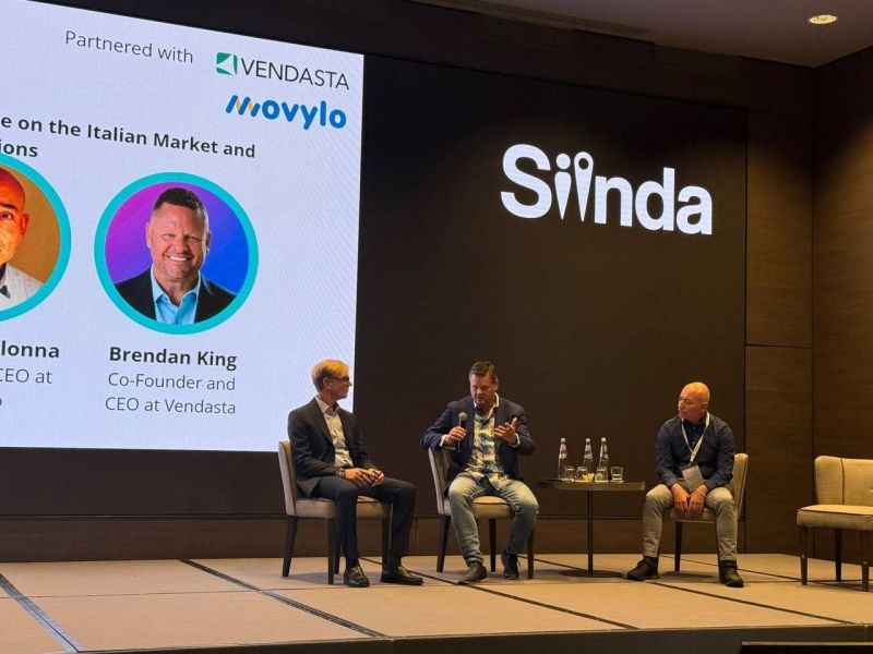 Brendan King, seated at centre, speaking into a microphone on a Siinda panel