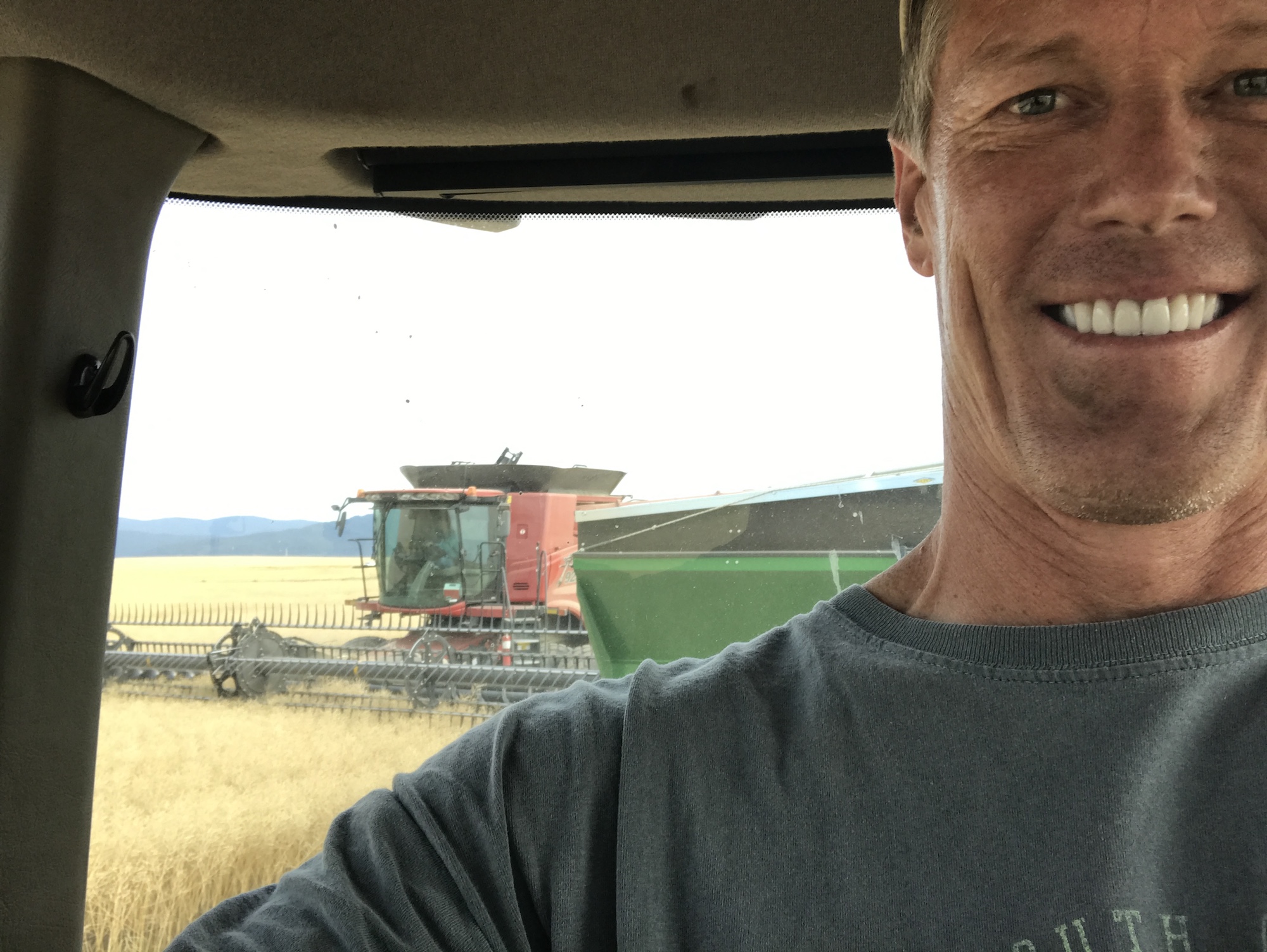 Brent Frei smiling from a farm vehicle, with harvesting machinery visible behind him