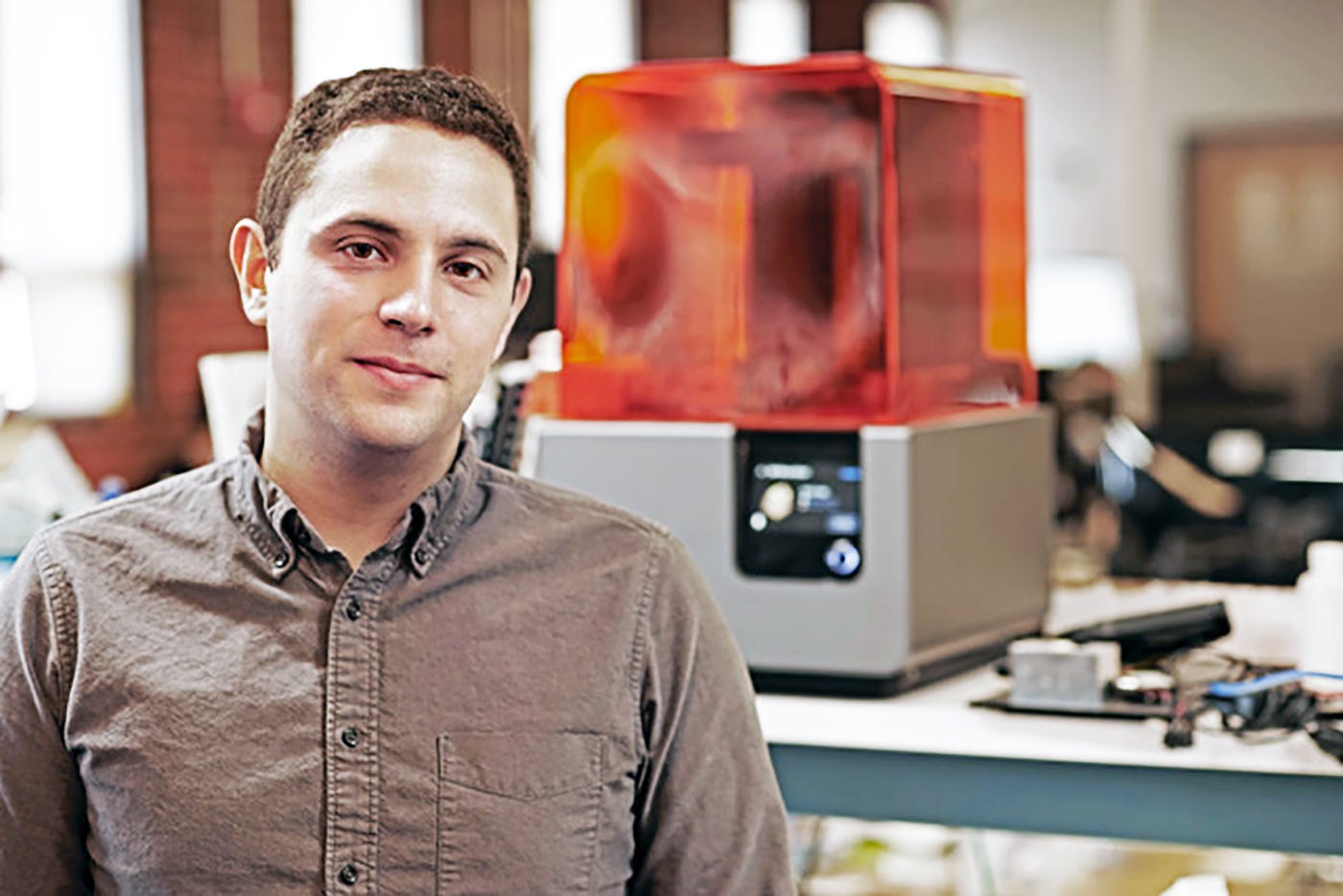 Brett Granberg seated in a workshop beside a desktop fabrication machine