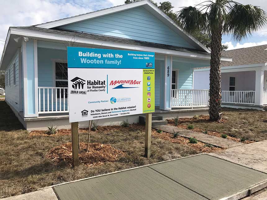 A blue Habitat for Humanity house with a MarineMax community partner sign