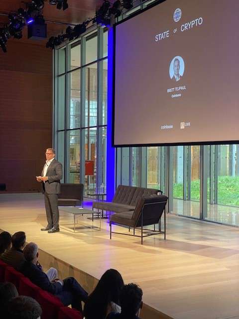 Brett Tejpaul speaking on stage beneath a State of Crypto screen