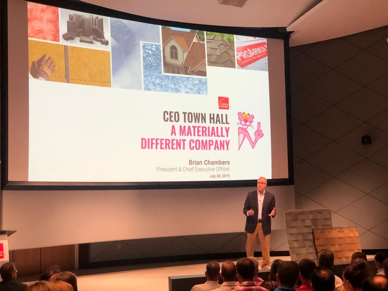 Brian Chambers speaking at a CEO town hall beside a display of roofing shingles, July 2019