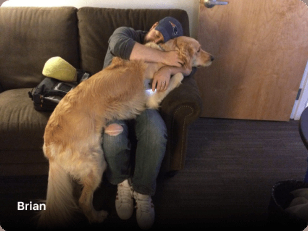 Brian Fox in a backward cap hugging a golden retriever on a sofa