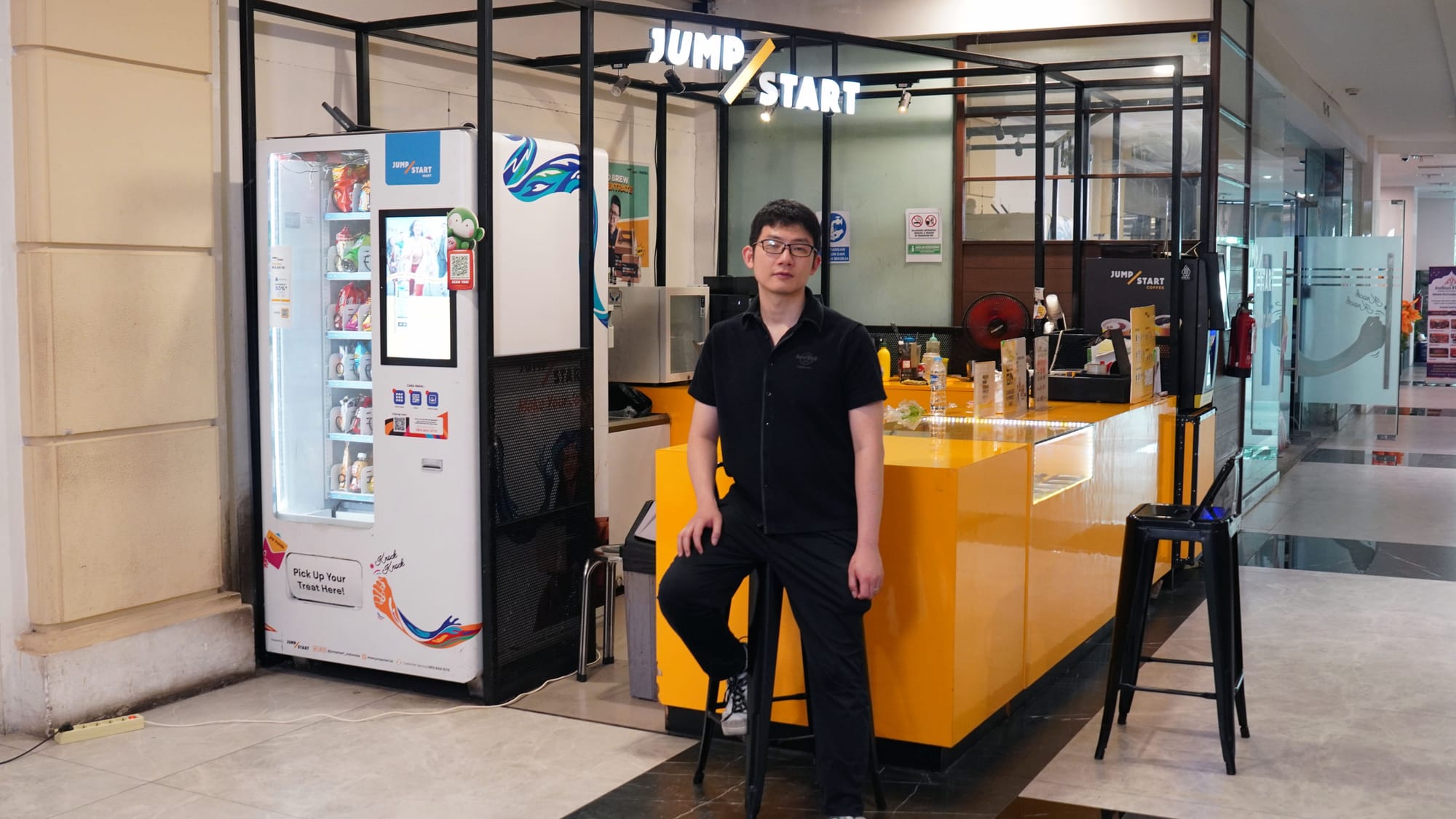 Brian Imawan beside a vending machine and yellow JumpStart counter in Jakarta