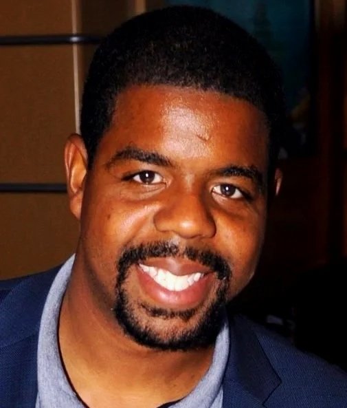 Brian Walker in a dark suit and tie, smiling against a neutral background