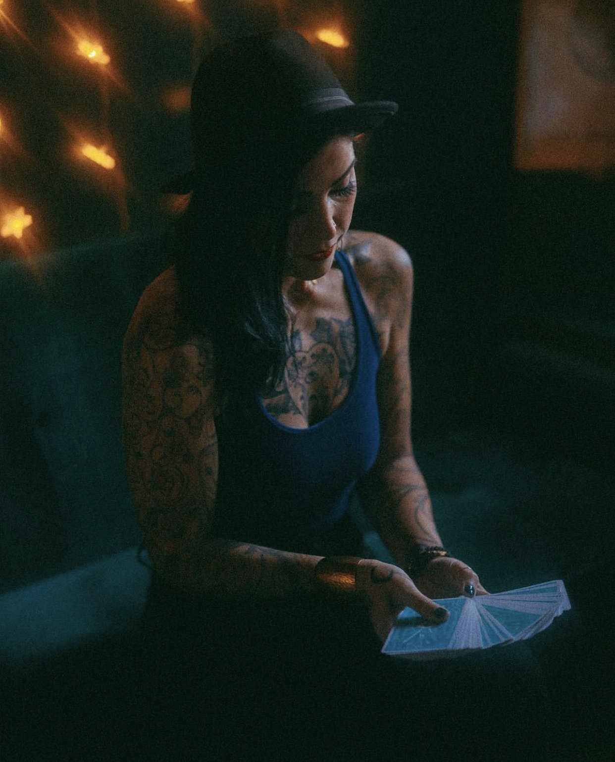 Brie James in a dark room, wearing a black hat and holding a fan of tarot cards