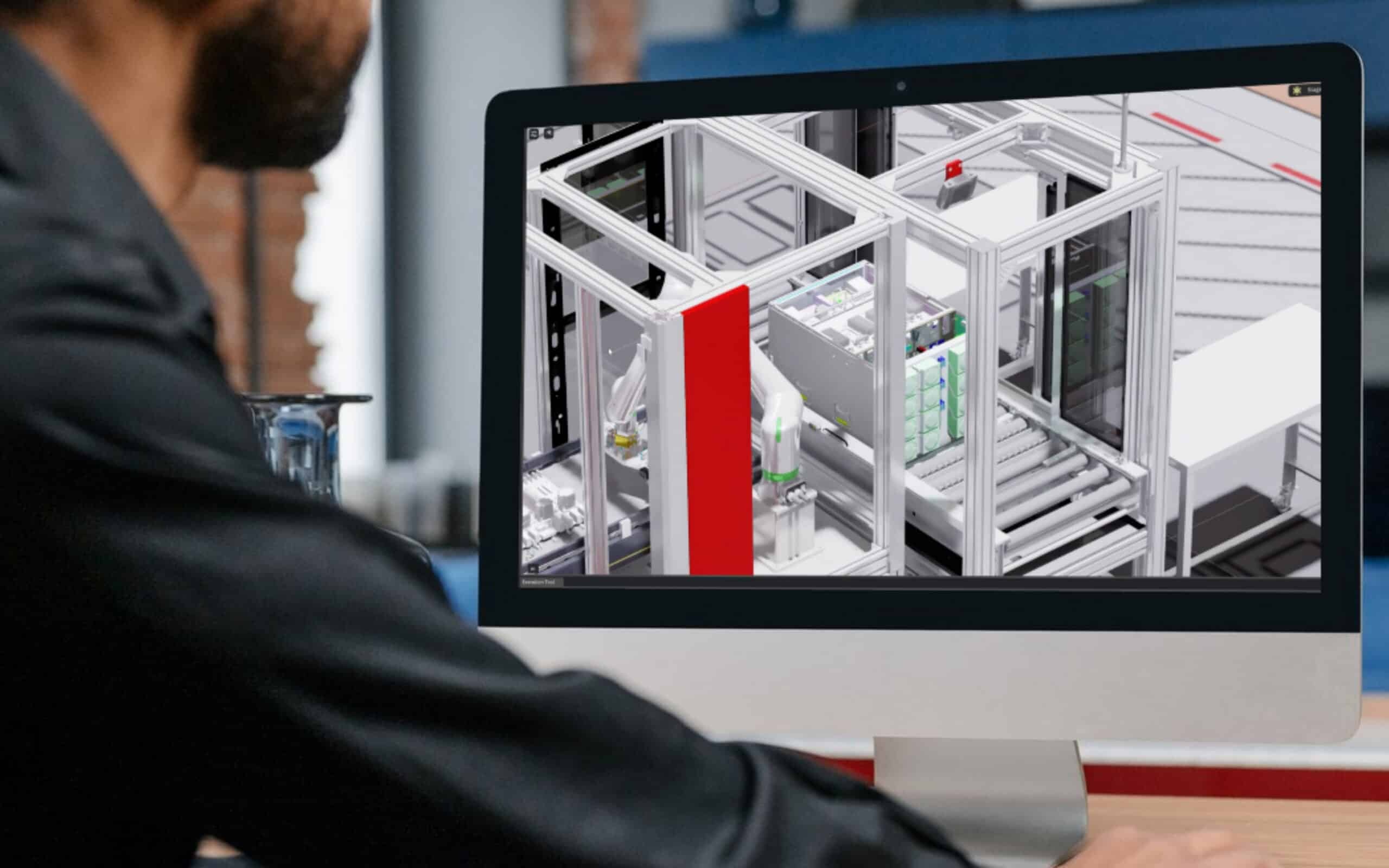 A person examines a digital model of robotic assembly cells on a desktop monitor