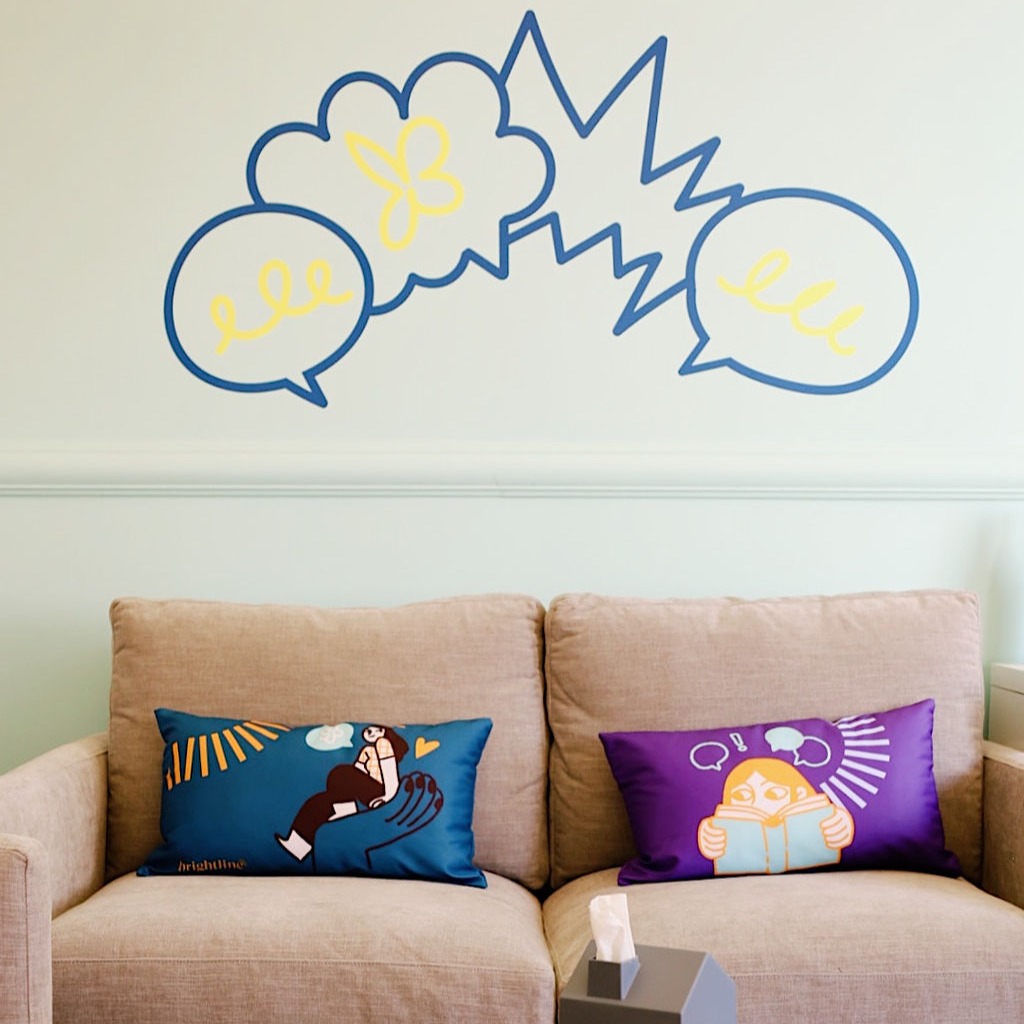 A sofa with colorful illustrated cushions beneath speech-bubble art in Brightline's Brooklyn clinic