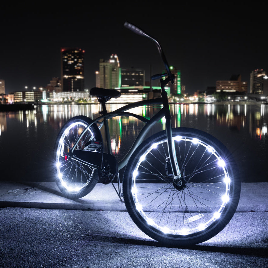 A bike wheel wrapped in glowing Brightz LED lights against a city skyline at night
