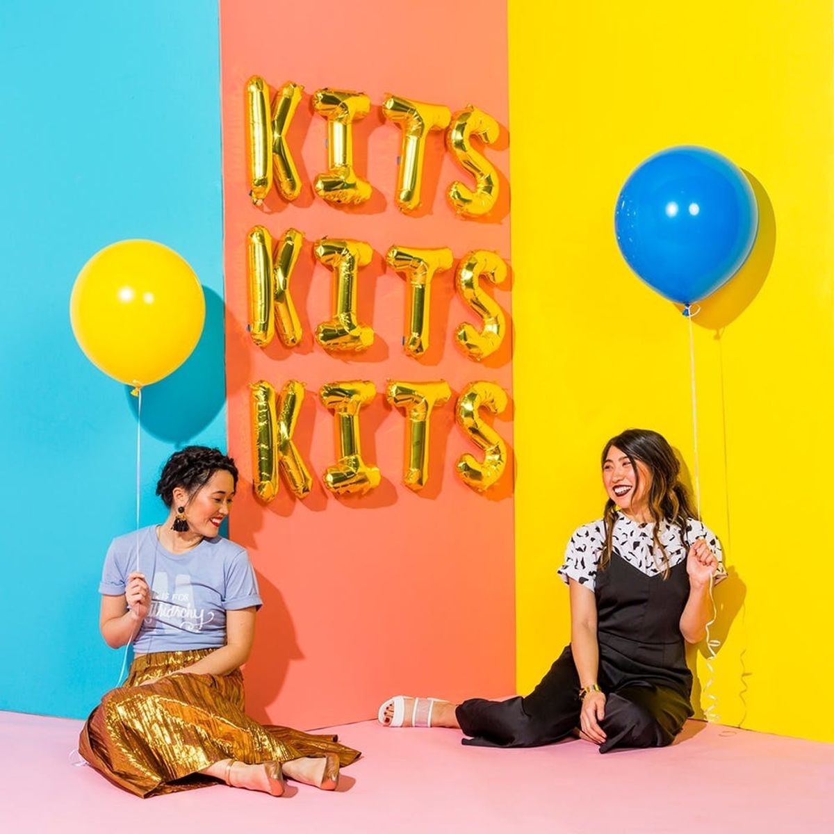 Two women celebrating the DIY kit launch with balloons against teal, orange and yellow panels