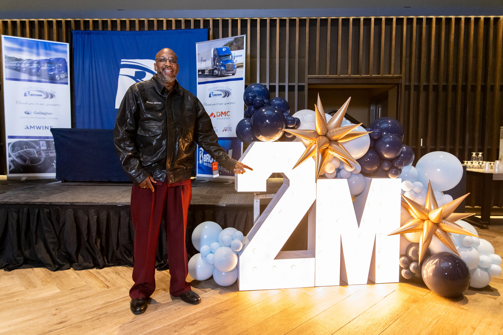 Tyrone Sanders beside a 2M sign at Brown’s 2025 Million Mile Hall of Fame celebration