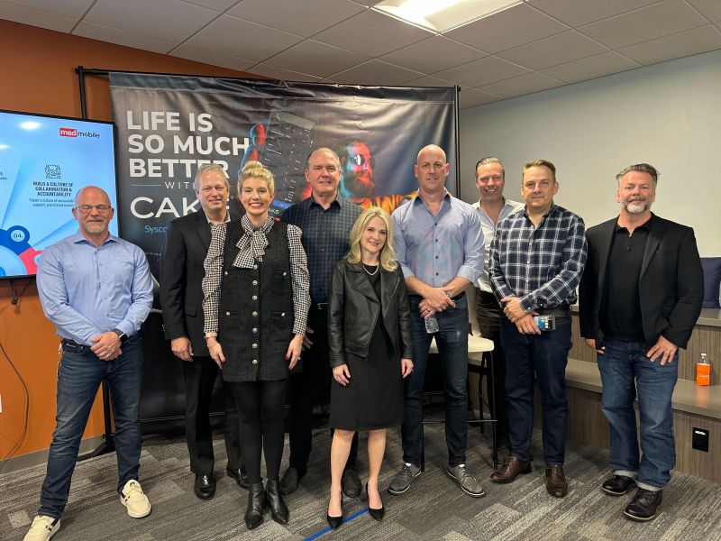 Mad Mobile leaders gathered in front of a CAKE display at the company’s 2025 all-hands meeting