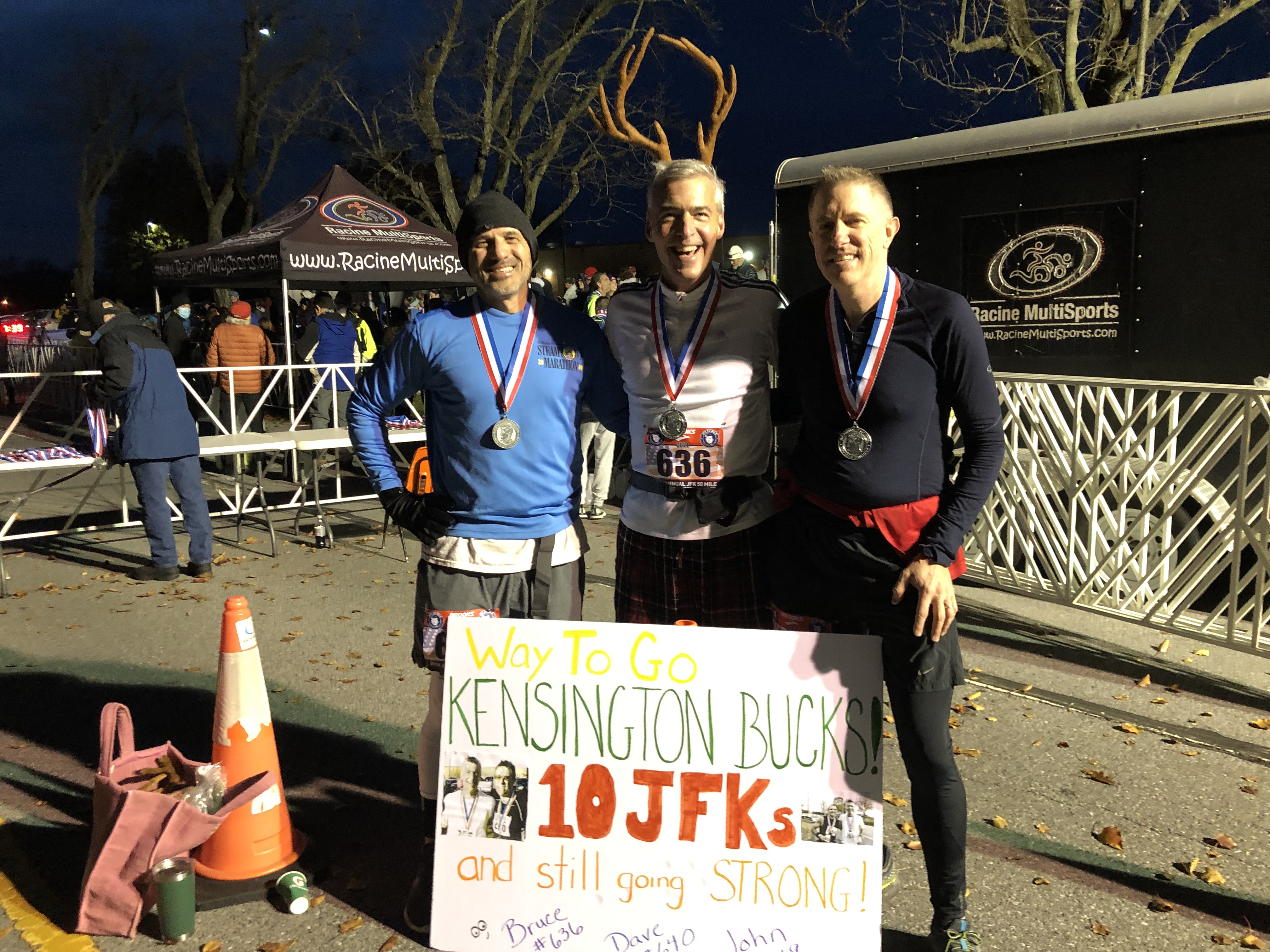 Caswell and his running partners at a race finish with medals and a Kensington Bucks sign