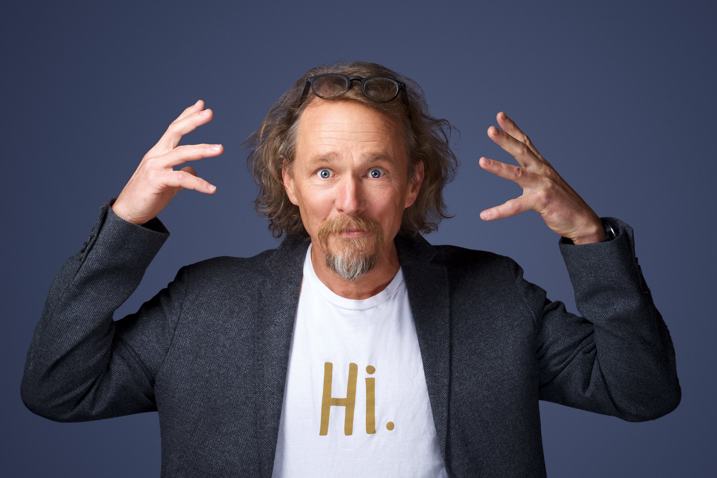 Bruce Linton raises both hands, with glasses resting on his head and a Hi T-shirt under his jacket.