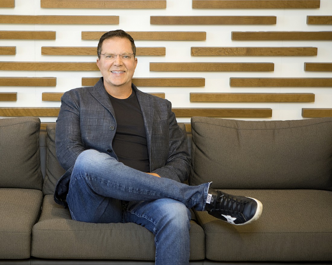 Bruce Lucas seated on a sofa, wearing a blazer, jeans and sneakers