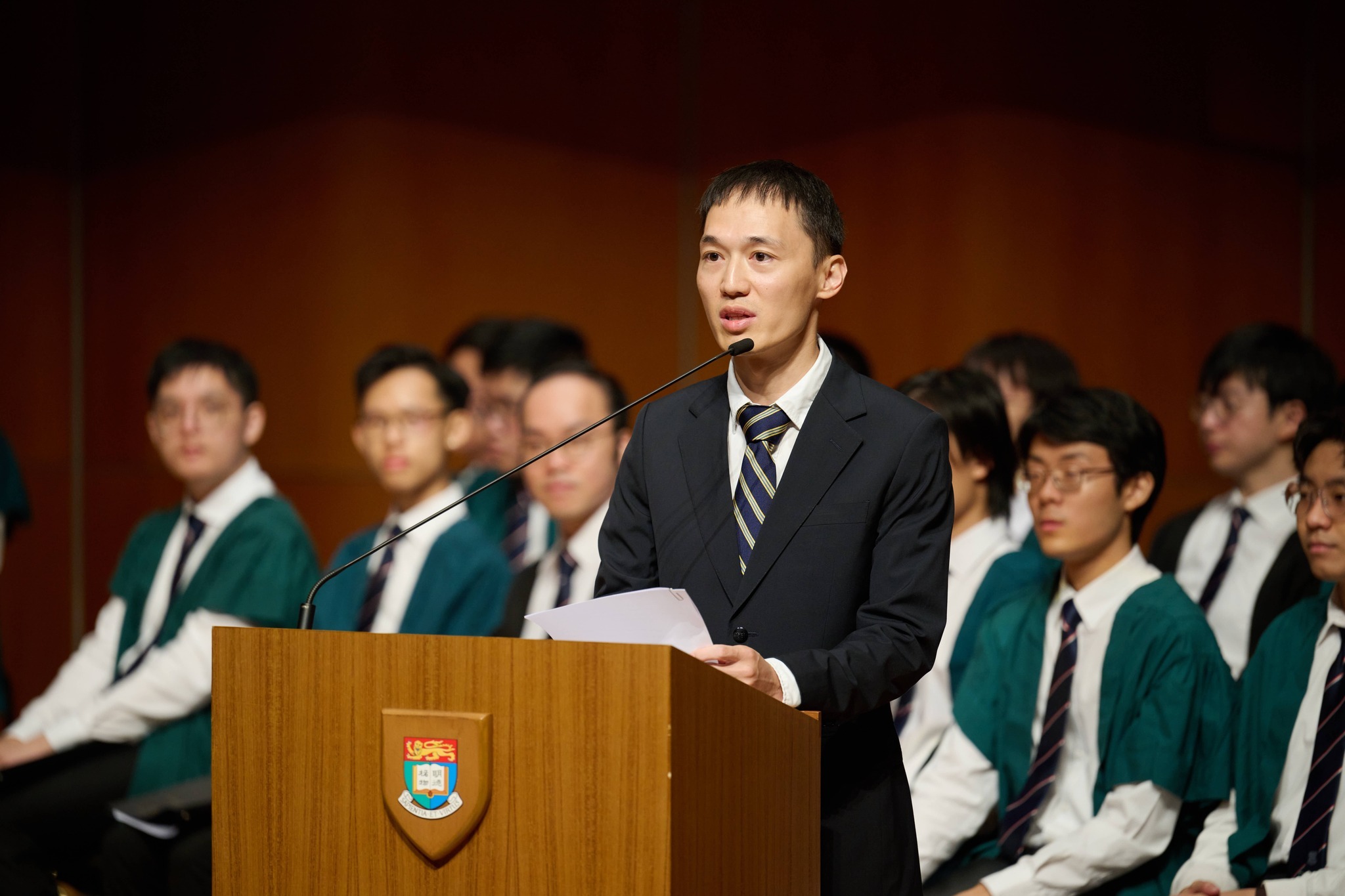 Bruce Wang speaking at a University of Hong Kong inauguration ceremony, with students behind him