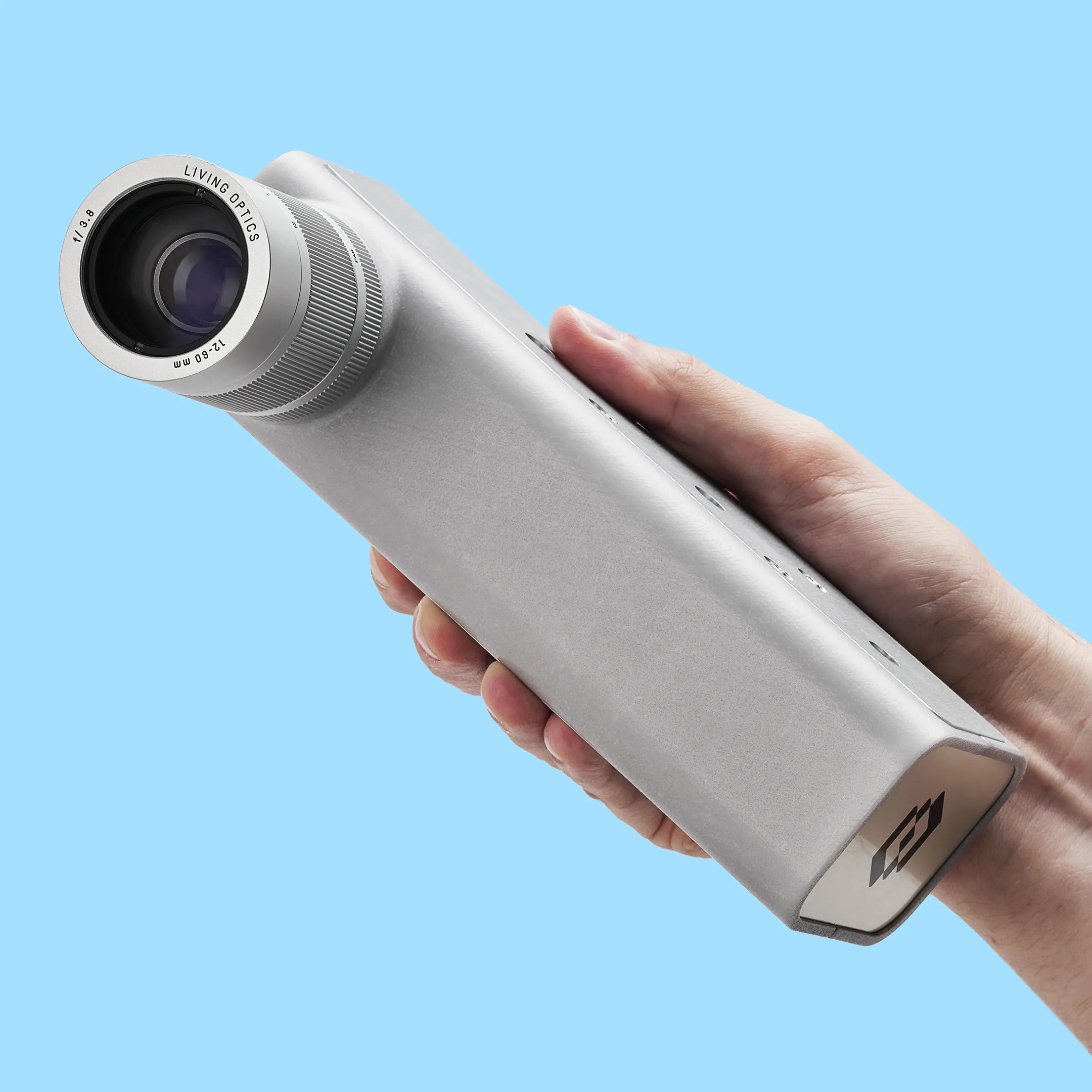 A hand holding the silver Living Optics hyperspectral camera against a pale blue background