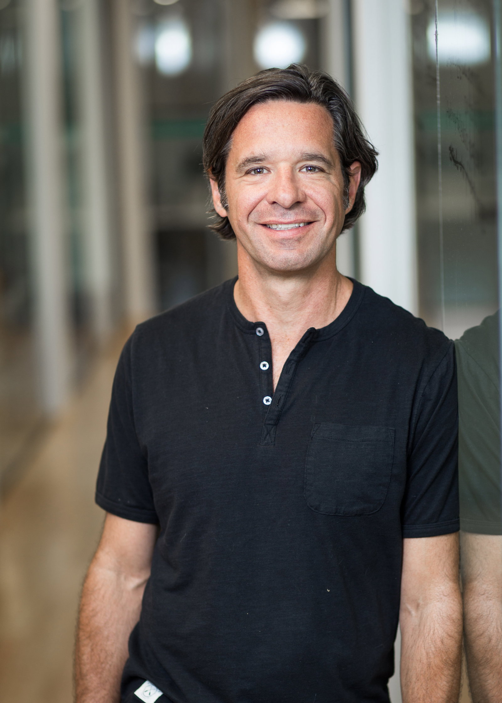 Bryan House in a black shirt, standing beside a reflective wall
