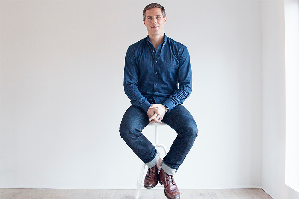 Bryan Mahoney seated on a stool in a bright studio during his Glossier years