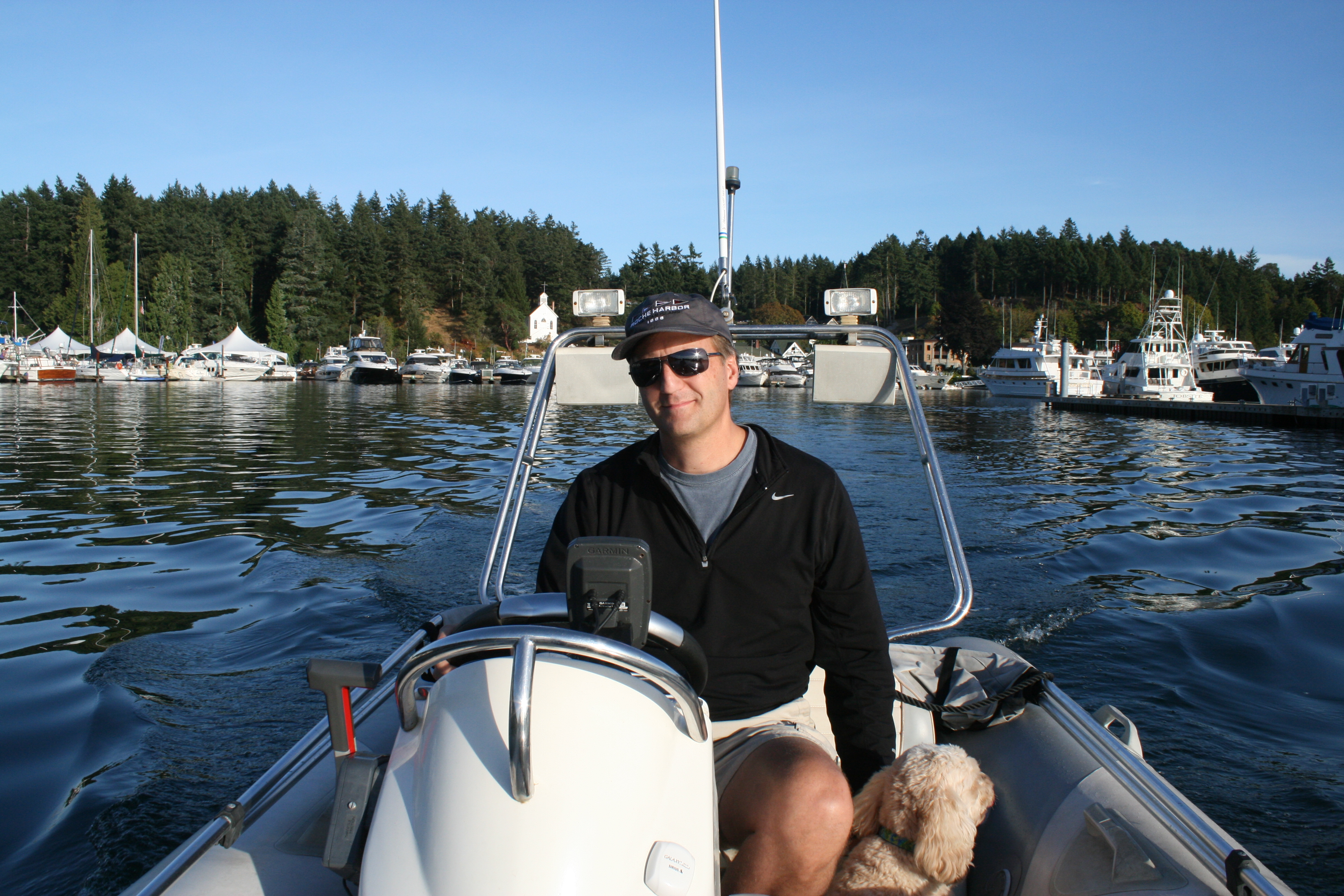 Bryan Mistele at the helm of a small boat with a dog beside him and a marina behind