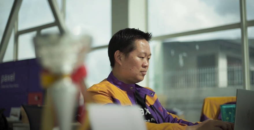 Bryant Christanto working at a desk in his purple and yellow Paxel jacket