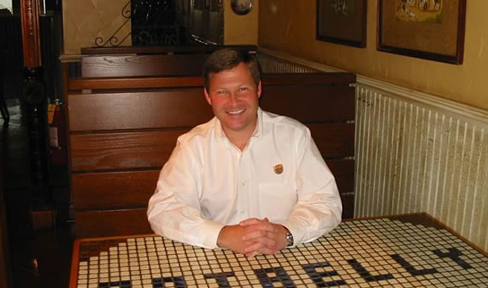 Bryant Keil seated in a Potbelly booth at a mosaic table spelling out the restaurant’s name