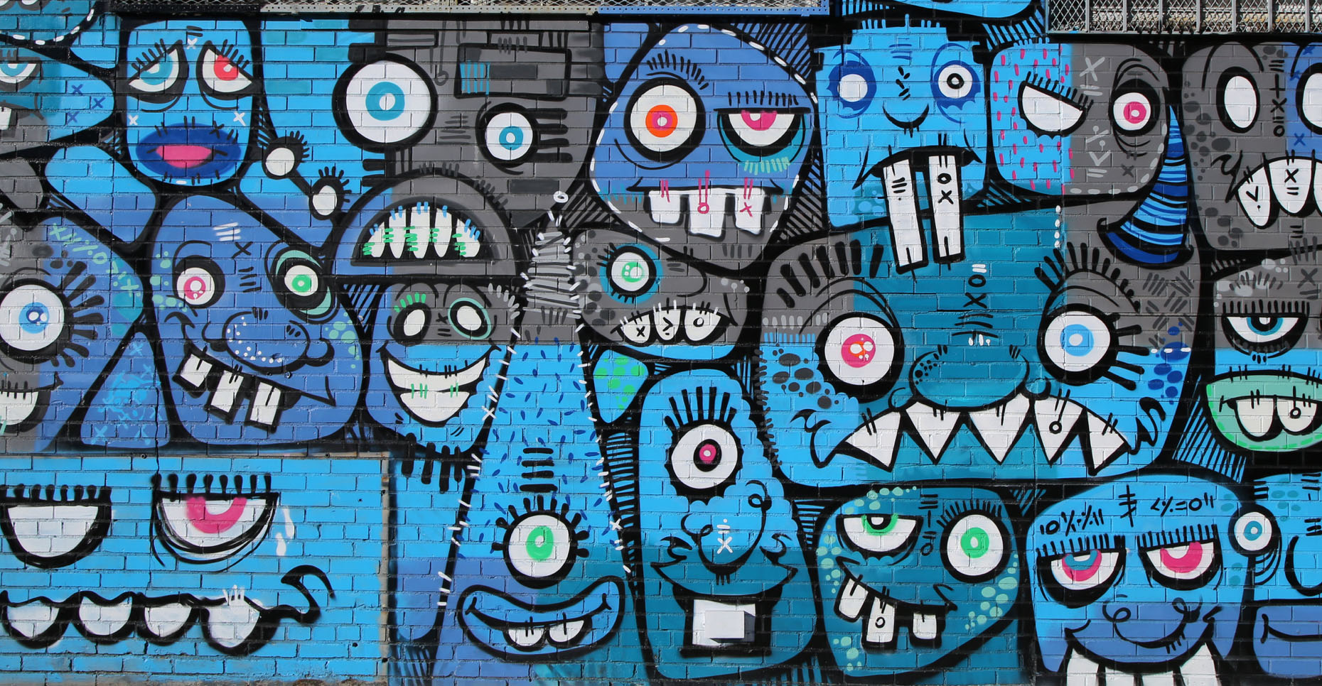 A colorful mural of playful blue and gray faces on a brick wall