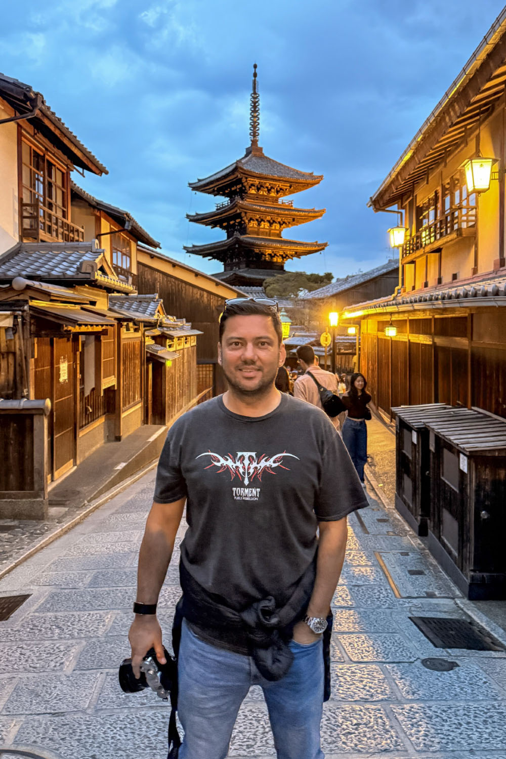 Burak Arik holding a camera on a lantern-lit street in Japan, with a pagoda behind him