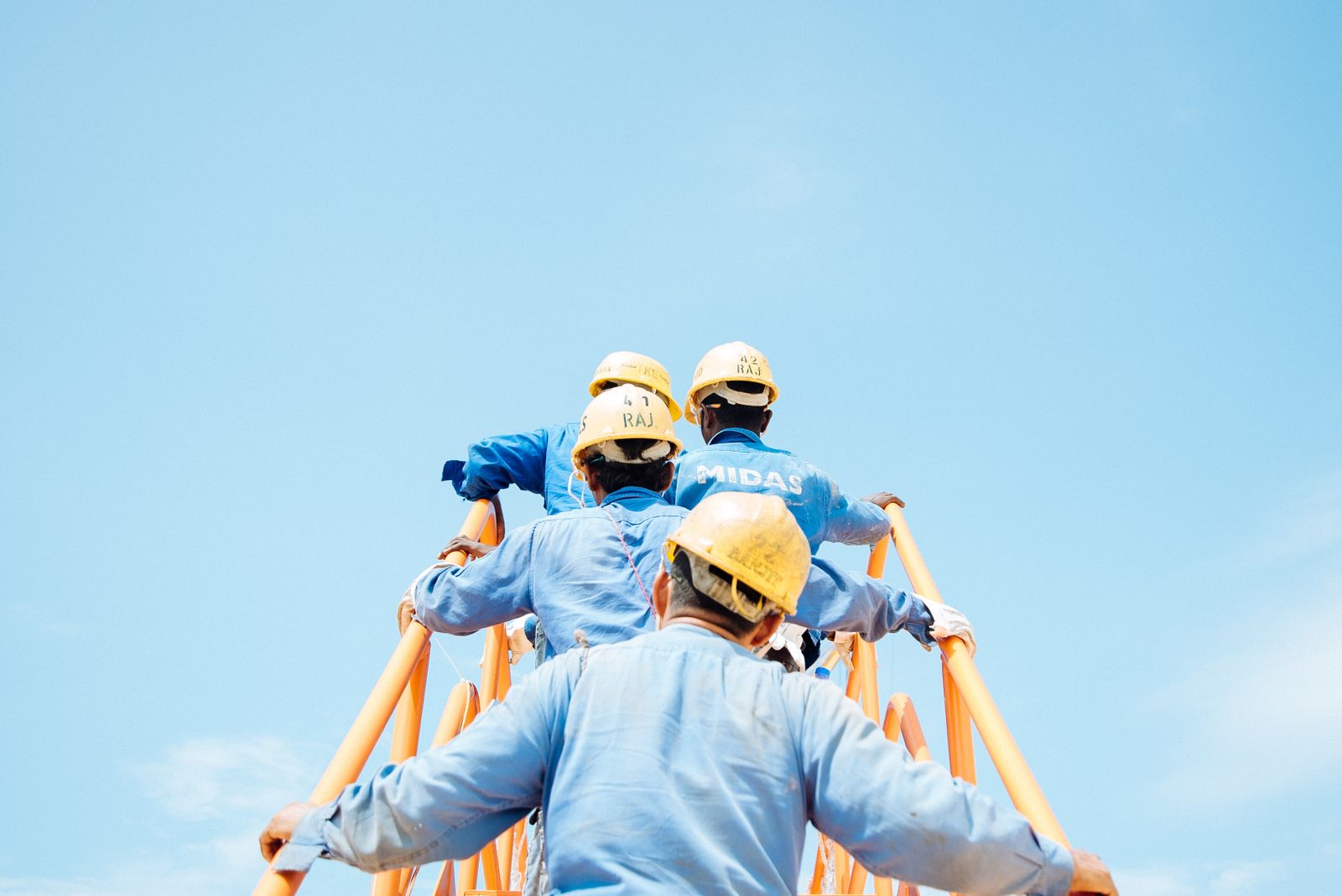 Construction workers in blue uniforms and yellow hard hats climbing a ladder