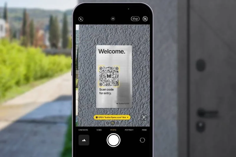 Phone camera scanning a ButterflyMX QR intercom plaque beside an entrance