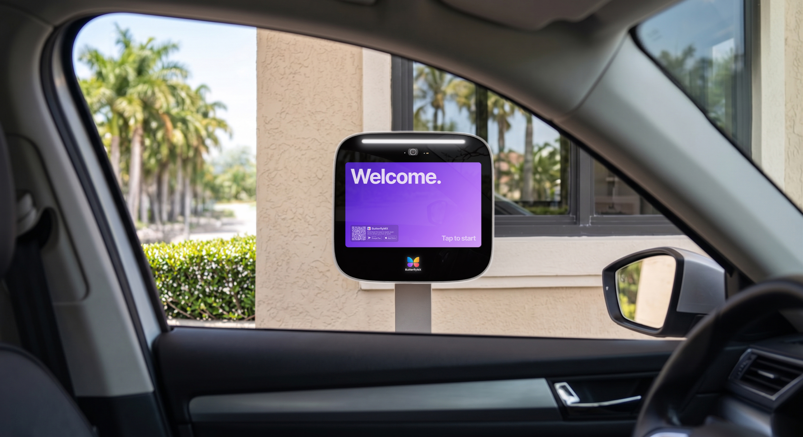 ButterflyMX touchscreen intercom on a pedestal, viewed through a car window