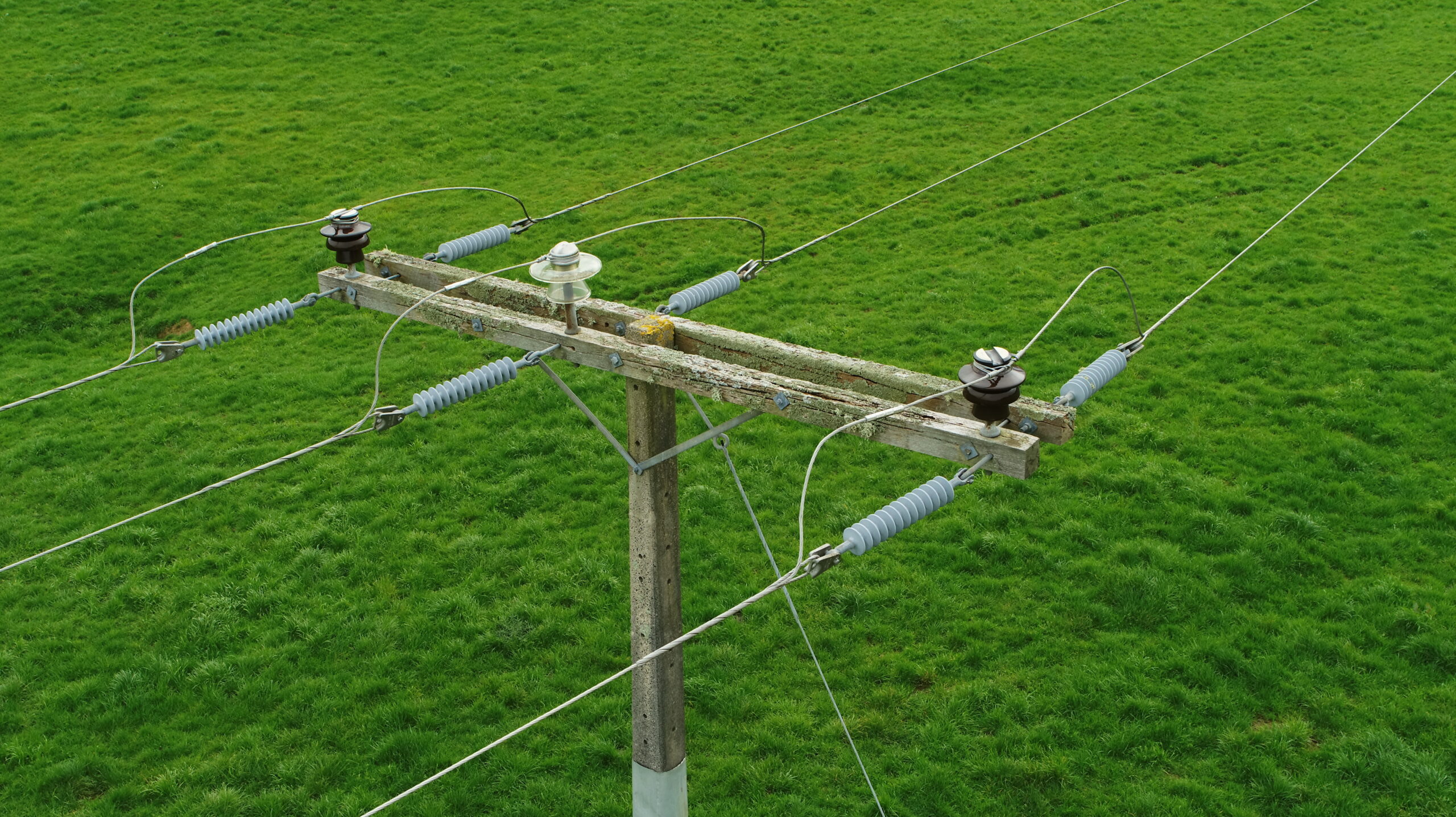 Aerial view of a utility pole and electrical hardware crossing a green field